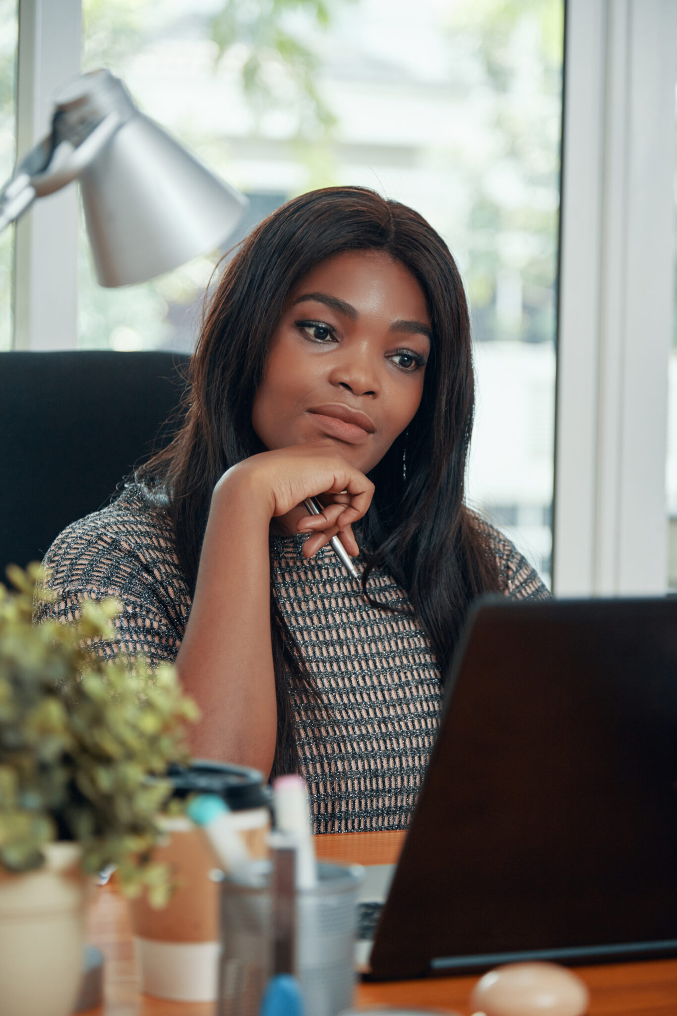 Beautiful black woman watching laptop pensively working at table in modern office